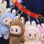 Multiple colorful Labubu plush keychains hanging on a red strap, worn across the shoulder.