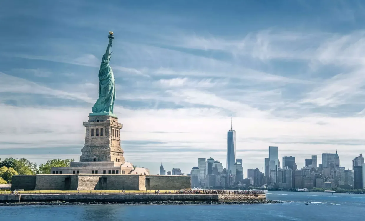 The Statue of Liberty standing tall on Liberty Island with the Manhattan skyline in the background.