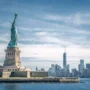 The Statue of Liberty standing tall on Liberty Island with the Manhattan skyline in the background.