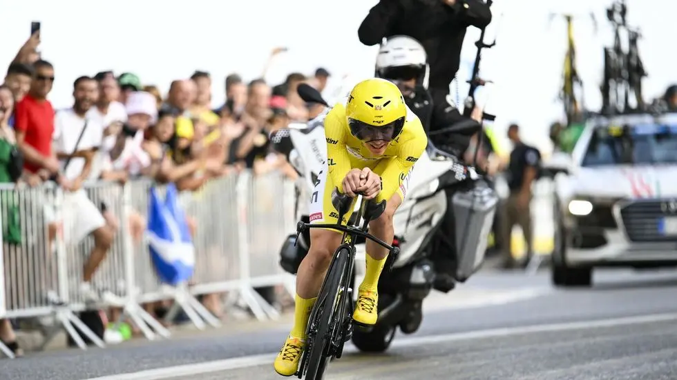 Cyclist in yellow jersey leading a time trial stage at Tour de France 2025, surrounded by cheering fans and team support vehicles.
