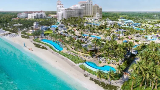 Aerial view of Baha Bay Water Park in Nassau, Bahamas, showing beachfront cabanas, winding pools, water slides, and luxury resort buildings surrounded by palm trees.