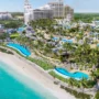 Aerial view of Baha Bay Water Park in Nassau, Bahamas, showing beachfront cabanas, winding pools, water slides, and luxury resort buildings surrounded by palm trees.
