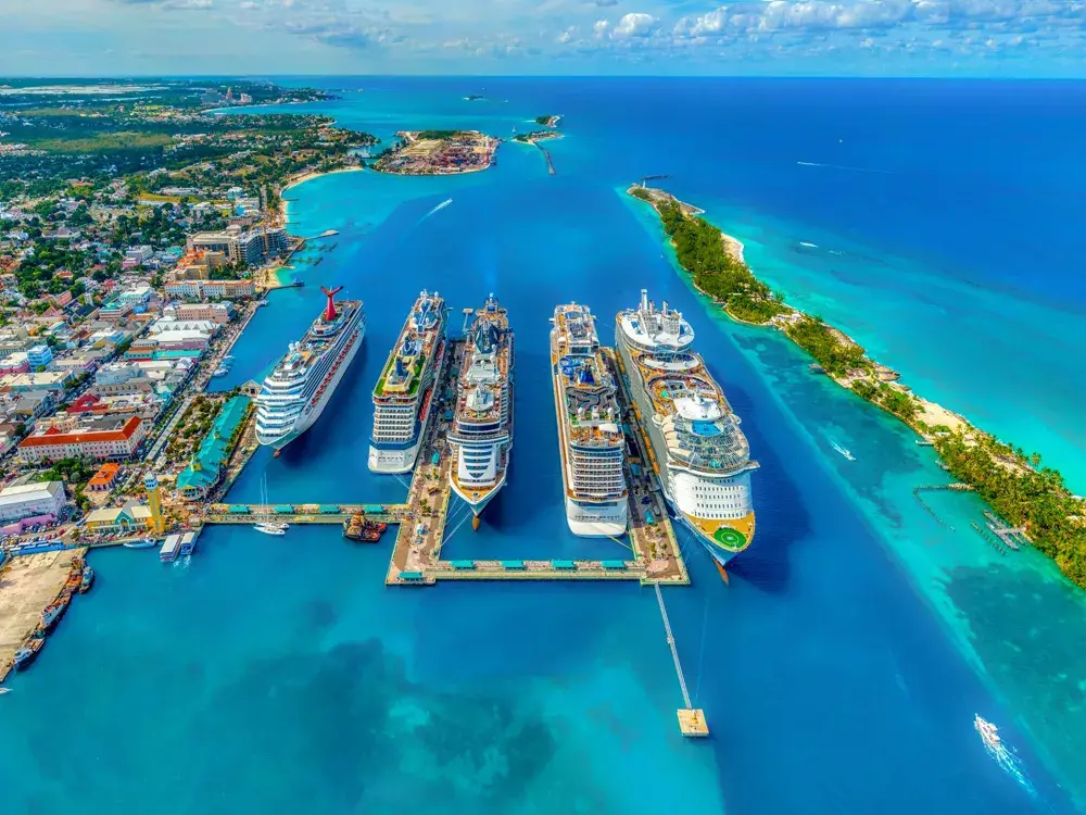 Aerial view of Nassau cruise port in the Bahamas with multiple docked ships, turquoise water, and nearby Paradise Island on a sunny day.