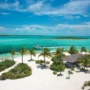 Aerial view of a secluded white sand beach with palm trees and turquoise waters in the Bahamas, perfect for luxury resort stays or island getaways.