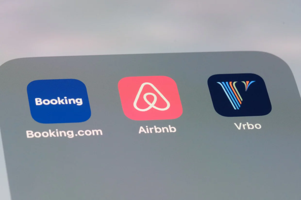 Three mobile app icons for Booking.com, Airbnb, and Vrbo are displayed side by side on a smartphone screen.