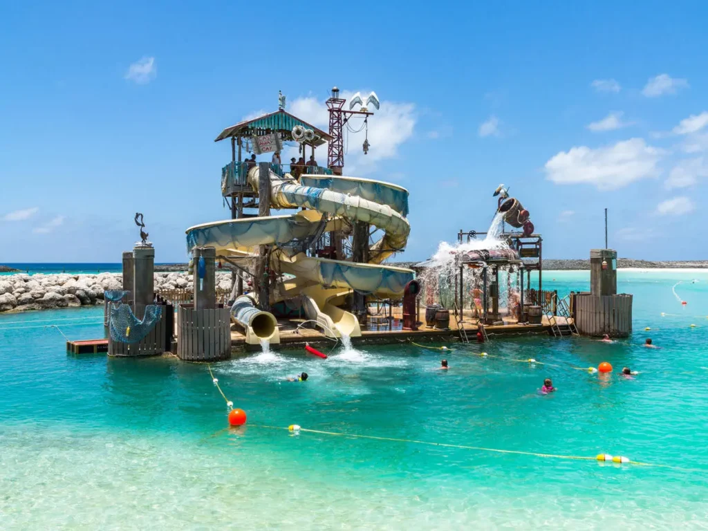 Floating water playground with slides and splash features at Castaway Cay in the Bahamas, surrounded by turquoise water and children swimming nearby.
