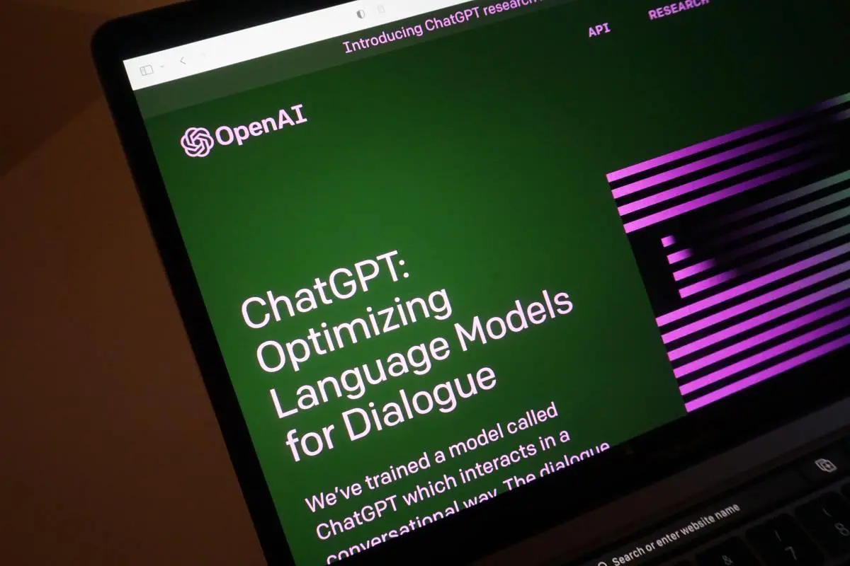 Laptop screen showing the OpenAI website with the title “ChatGPT: Optimizing Language Models for Dialogue” on a green background with purple accents.