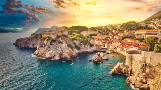 Scenic aerial view of Dubrovnik Old Town and fortress at sunset, with kayaks in the turquoise Adriatic Sea and dramatic clouds above the coastline.
