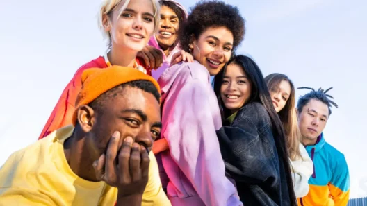 A diverse group of smiling Gen Z friends wearing colorful streetwear, standing close together outdoors on a sunny day, radiating youthful energy and positivity.