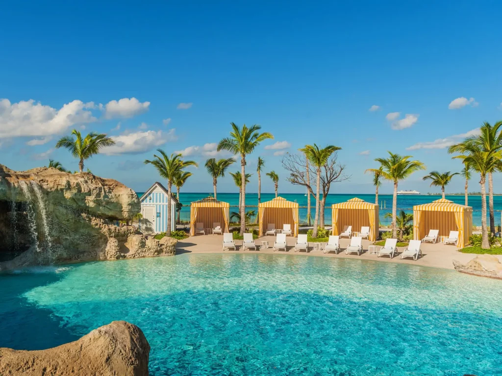 Yellow-striped cabanas and lounge chairs beside a tropical pool overlooking the ocean at Grand Hyatt Baha Mar.
