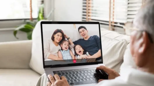 Elderly person video calling their family on a laptop, showing a happy family with two children smiling on the screen during a virtual conversation.