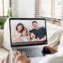 Elderly person video calling their family on a laptop, showing a happy family with two children smiling on the screen during a virtual conversation.