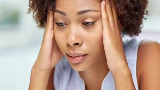 Woman holding her head with both hands, appearing fatigued and in pain—suggesting symptoms of a migraine or intense headache.