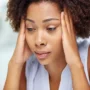 Woman holding her head with both hands, appearing fatigued and in pain—suggesting symptoms of a migraine or intense headache.