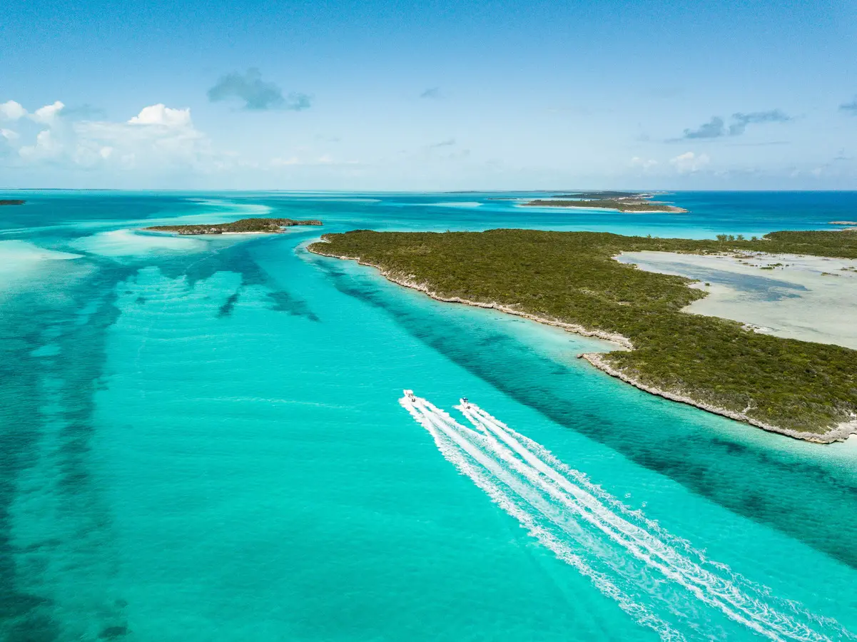 Crystal-clear turquoise water and small islets with speedboats leaving trails near Nassau, Bahamas.