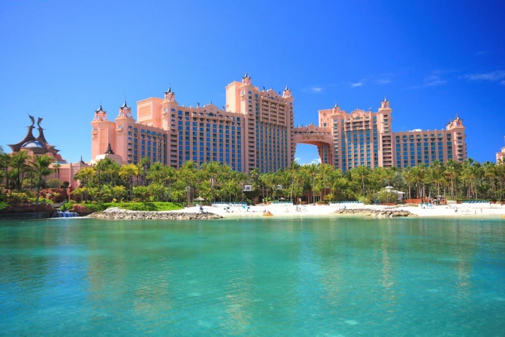 Front view of Atlantis Paradise Island resort in the Bahamas, with its iconic pink towers, lush palm trees, and turquoise lagoon under a bright blue sky.