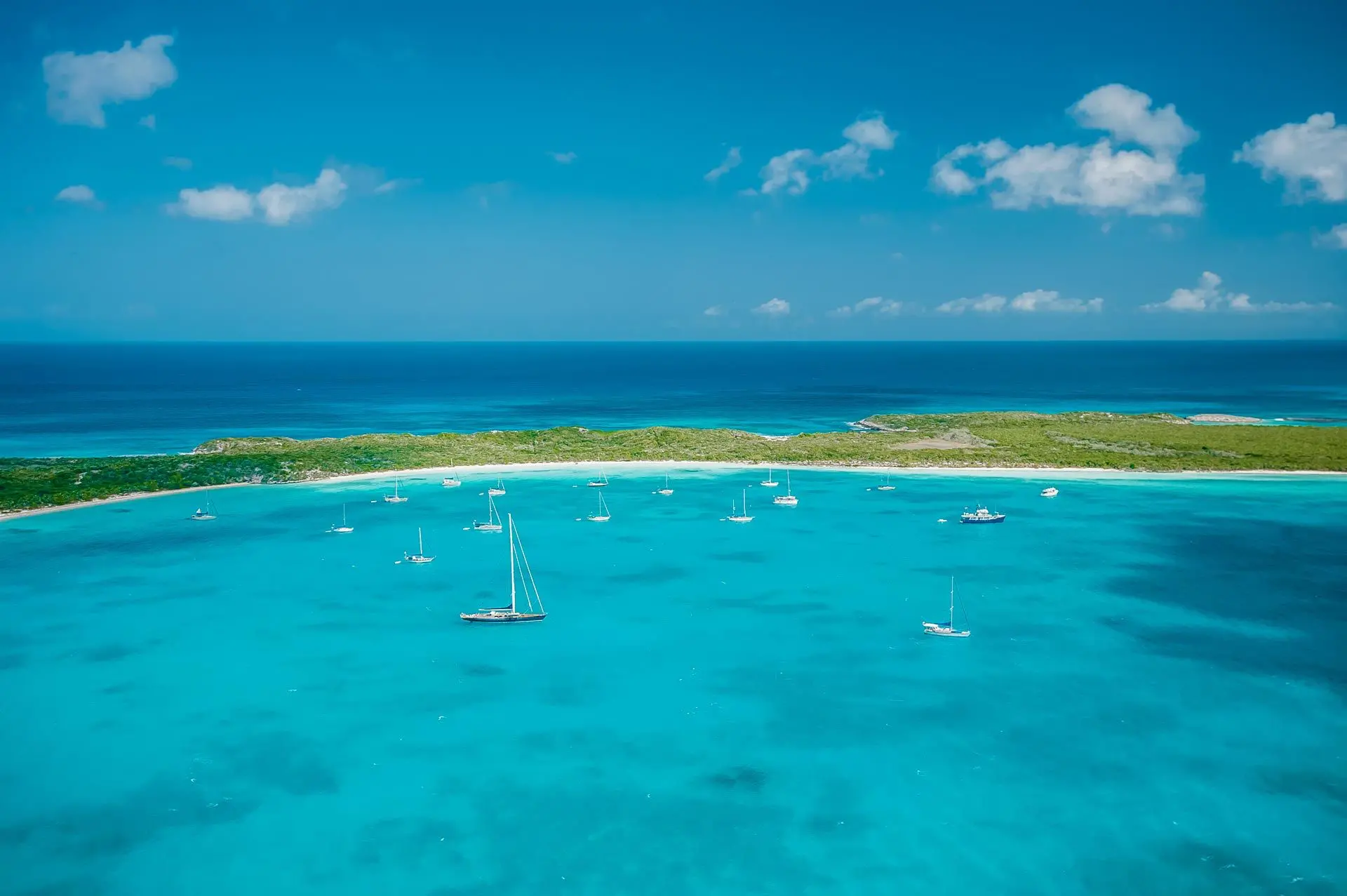 Scenic view of turquoise waters and sailboats anchored near a remote island in the Bahamas under clear blue skies.