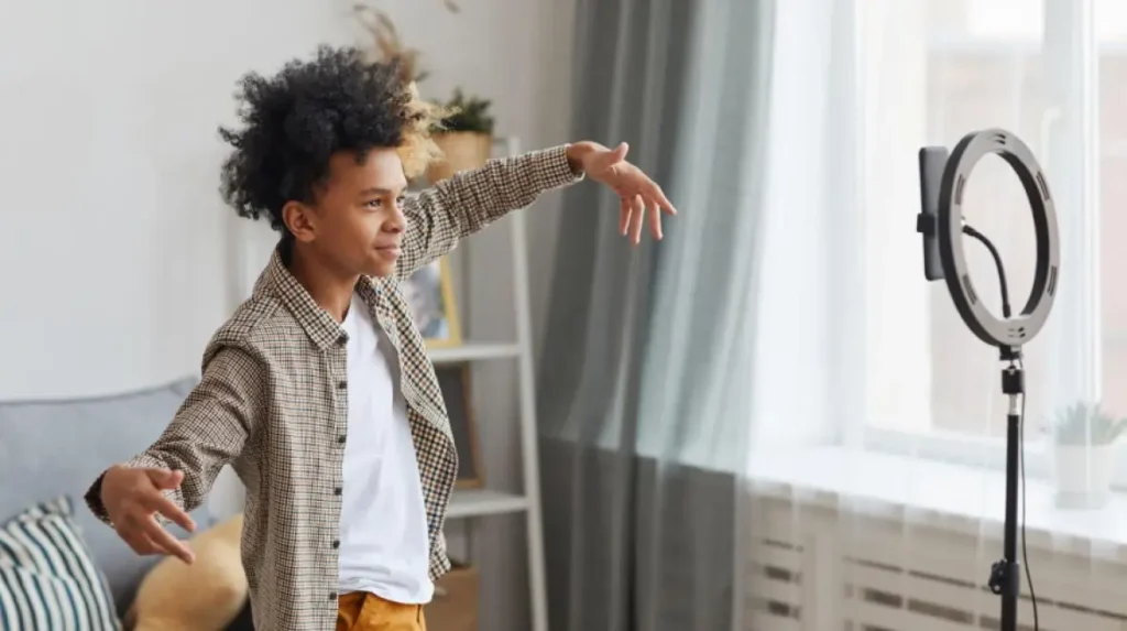 A young boy recording a TikTok dance video at home using a smartphone and ring light, highlighting children’s active use of social media platforms.