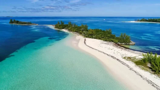 Aerial view of a pristine white sand beach and turquoise waters on a tropical island in the Bahamas, surrounded by lush greenery and calm ocean bays.