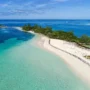 Aerial view of a pristine white sand beach and turquoise waters on a tropical island in the Bahamas, surrounded by lush greenery and calm ocean bays.
