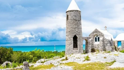 Stone monastery of Mount Alvernia on Cat Island, Bahamas, with a white conical tower and panoramic ocean view under a dramatic cloudy sky.