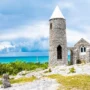 Stone monastery of Mount Alvernia on Cat Island, Bahamas, with a white conical tower and panoramic ocean view under a dramatic cloudy sky.