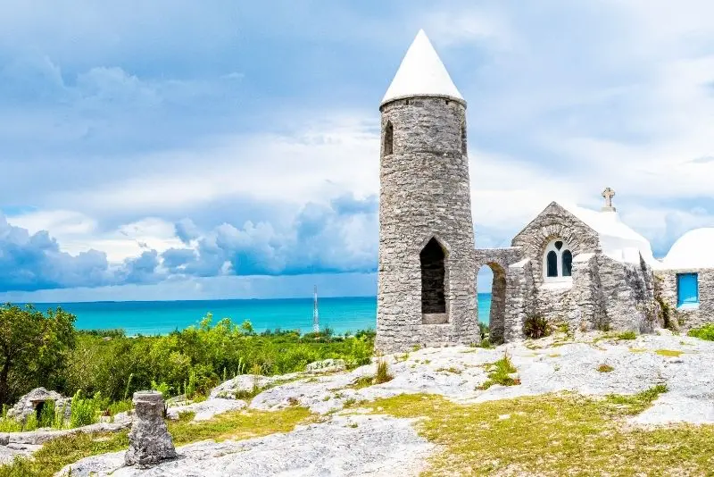 Stone monastery of Mount Alvernia on Cat Island, Bahamas, with a white conical tower and panoramic ocean view under a dramatic cloudy sky.