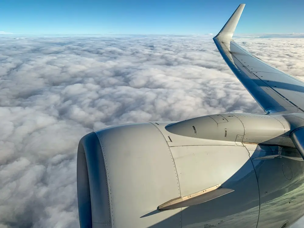 View from an airplane window showing the wing, engine, and a beautiful sky full of clouds during flight.