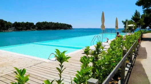 Infinity pool at Crvena Luka Resort in Croatia, with sun loungers and umbrellas overlooking the turquoise sea and lush coastline on a sunny day.