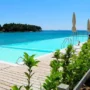 Infinity pool at Crvena Luka Resort in Croatia, with sun loungers and umbrellas overlooking the turquoise sea and lush coastline on a sunny day.