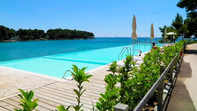 Infinity pool at Crvena Luka Resort in Croatia, with sun loungers and umbrellas overlooking the turquoise sea and lush coastline on a sunny day.