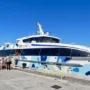 A group of travelers boarding a modern TP Line ferry named Proversa at the dock in Split, Croatia, under a bright blue sky, ready for a trip to Hvar.