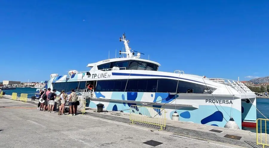 A group of travelers boarding a modern TP Line ferry named Proversa at the dock in Split, Croatia, under a bright blue sky, ready for a trip to Hvar.