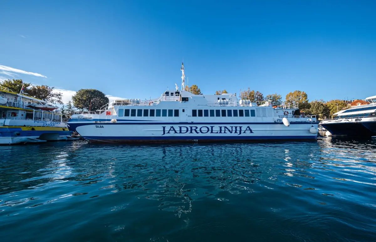 The Jadrolinija ferry named Silba docked at the harbor in Croatia, with calm blue water and clear skies, ready for passengers to travel between the islands.