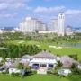 Aerial view of Royal Blue Golf Club with the iconic Baha Mar resort in the background, surrounded by palm trees, water features, and lush greenery in Nassau, The Bahamas.