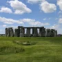 View of Stonehenge on a sunny day in Wiltshire, England, with clear skies, green grass, and tourists walking in the distance.