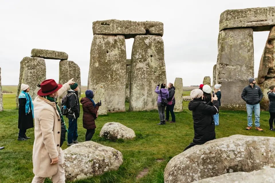 Tourists exploring the inner circle of Stonehenge on a cloudy day, with people taking photos and observing the ancient stones up close.