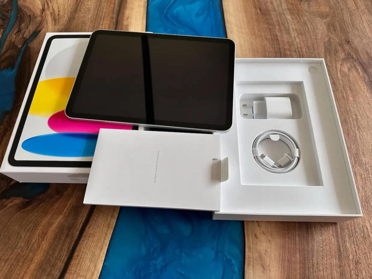 10th generation iPad unboxed on a wooden table, with charger and cable in clean white packaging.