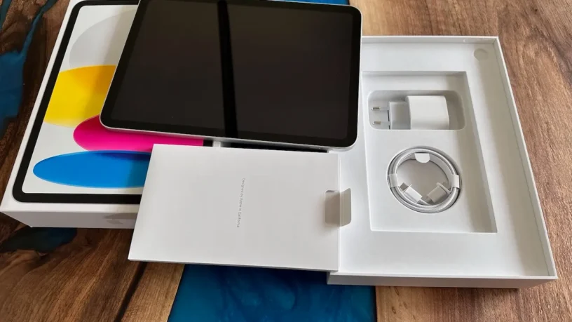 10th generation iPad unboxed on a wooden table, with charger and cable in clean white packaging.