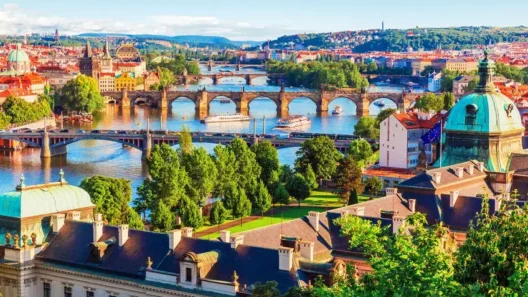 Scenic view of Prague with multiple historic bridges crossing the Vltava River, surrounded by colorful buildings, trees, and iconic architecture on a sunny day.