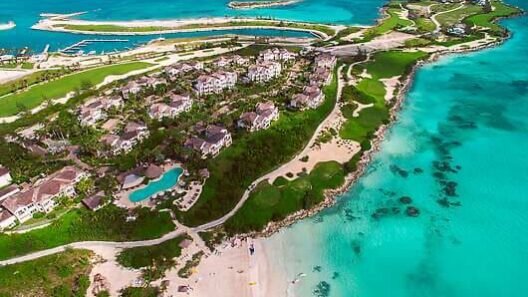 Aerial view of a luxury beachfront resort in the Bahamas, surrounded by lush greenery, white sandy beaches, turquoise ocean, and private villas—an idyllic Instagrammable spot perfect for capturing paradise moments on a tropical getaway.