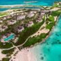 Aerial view of a luxury beachfront resort in the Bahamas, surrounded by lush greenery, white sandy beaches, turquoise ocean, and private villas—an idyllic Instagrammable spot perfect for capturing paradise moments on a tropical getaway.