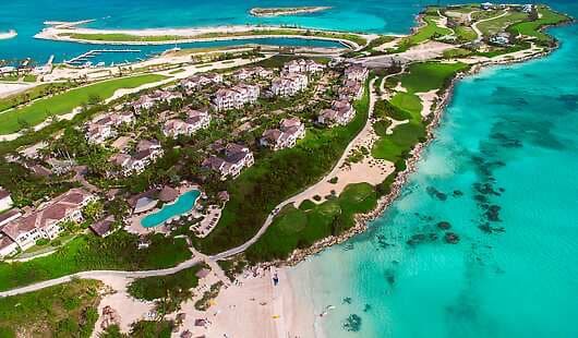 Aerial view of a luxury beachfront resort in the Bahamas, surrounded by lush greenery, white sandy beaches, turquoise ocean, and private villas—an idyllic Instagrammable spot perfect for capturing paradise moments on a tropical getaway.