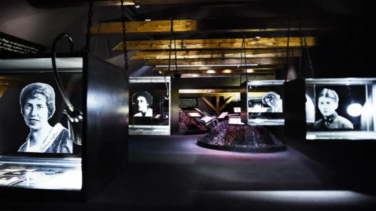 Interior view of the Franz Kafka Museum in Prague, showcasing illuminated display cases with black-and-white portraits and historical documents under wooden ceiling beams.
