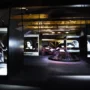 Interior view of the Franz Kafka Museum in Prague, showcasing illuminated display cases with black-and-white portraits and historical documents under wooden ceiling beams.