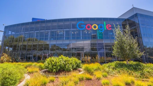 Modern Google headquarters with a colorful logo on a glass building, surrounded by green landscaping and blue sky in Mountain View, California.