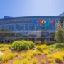 Modern Google headquarters with a colorful logo on a glass building, surrounded by green landscaping and blue sky in Mountain View, California.