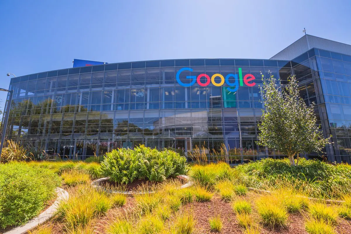 Modern Google headquarters with a colorful logo on a glass building, surrounded by green landscaping and blue sky in Mountain View, California.
