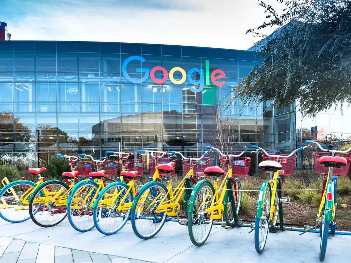 Colorful Google bikes parked in front of the Google headquarters with a glass facade and Google logo in Mountain View, California.