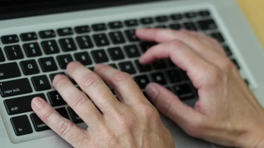 Close-up of hands typing on a laptop keyboard, representing searching or managing personal information online.